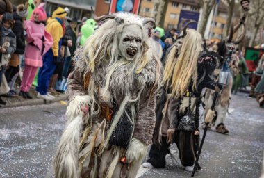 Zug, İsviçre - 1 Mart 2025: Tschaggatta, tüylü canavar kostümü giymiş biri İsviçre kış karnavalı Fasnacht geçit töreninde boynuzlu ahşap maske takıyor.