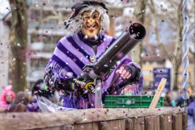 Zug, İsviçre - 1 Mart 2025 Fasnacht kış karnaval geçidinde elinde bir konfeti tabancasıyla cadı kıyafeti ve maske giymiş bir kostümcü