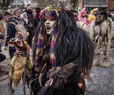 Zug, İsviçre - 1 Mart 2025: Tschaggatta, tüylü canavar kostümü giymiş biri İsviçre kış karnavalı Fasnacht geçit töreninde boynuzlu ahşap maske takıyor.