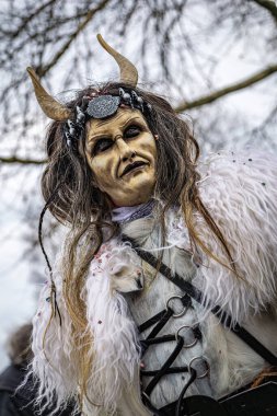 Zug, İsviçre - 1 Mart 2025: Tschaggatta, tüylü canavar kostümü giymiş biri İsviçre kış karnavalı Fasnacht geçit töreninde boynuzlu ahşap maske takıyor.