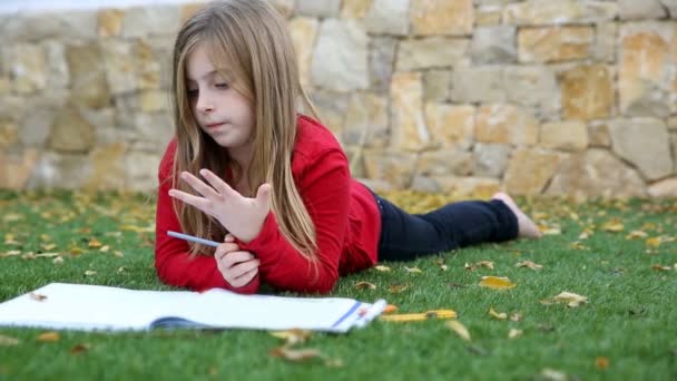 Блондинка девочка математика домашнее задание лежа на траве — стоковое видео