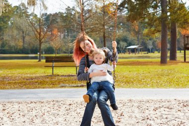 Mother and daughter in a swing at the park clipart