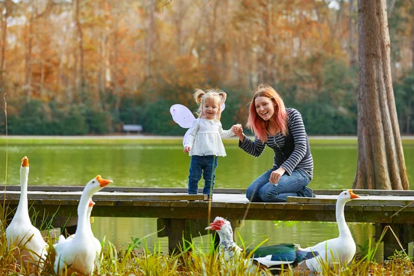 Kid girl and mother playing with ducks in lake — Stock Photo, Image