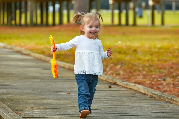 Miúdo bebê menina com brinquedo guitarra andando no parque — Fotografia de Stock