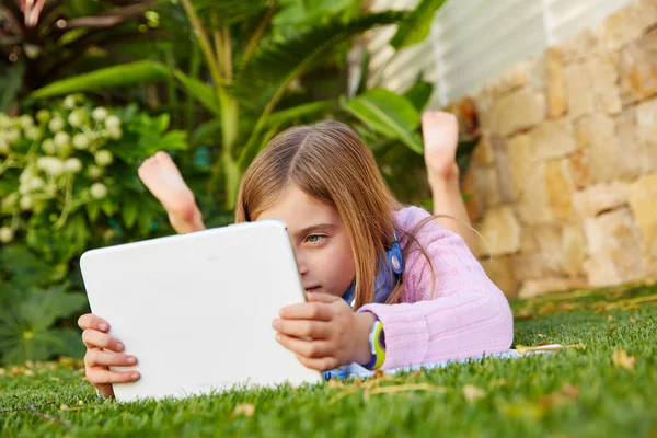 Menina criança loira com tablet pc deitado no relvado de grama — Fotografia de Stock