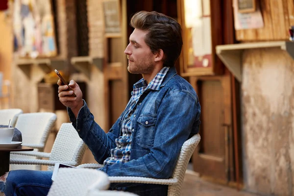 Молодий чоловік зі смартфоном у відкритому кафе — стокове фото