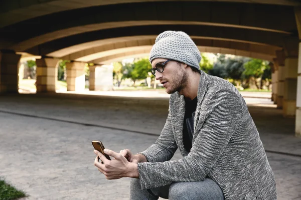 Jovem moderno com smartphone sob ponte — Fotografia de Stock