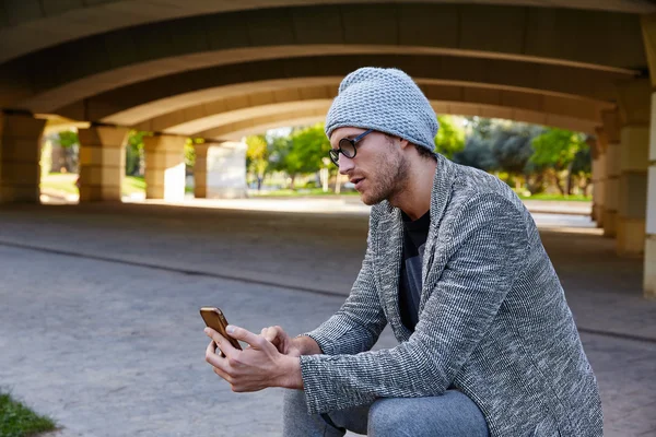 Современный молодой человек со смартфоном под мостом — стоковое фото