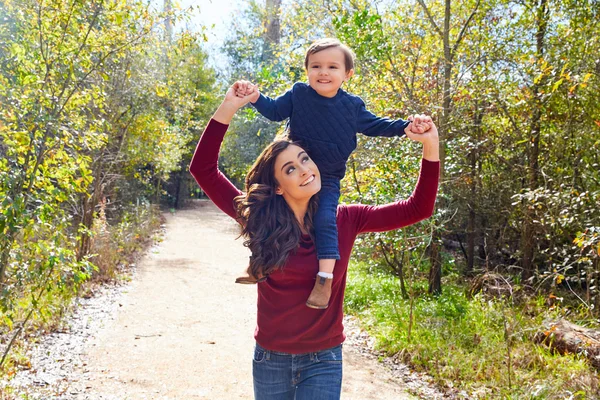 Bambino ragazzo sedersi su madre spalle a piedi parco — Foto Stock