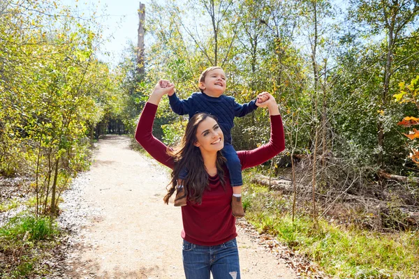 Unge pojke sitta på mor axlar promenader park — Stockfoto