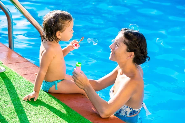 Bebé chica soplando bolas de jabón con madre en la piscina — Foto de Stock