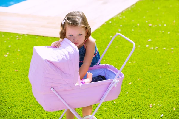 Дитяча дівчинка Тоддлер грає з дитячим візком у зеленому дерні — стокове фото