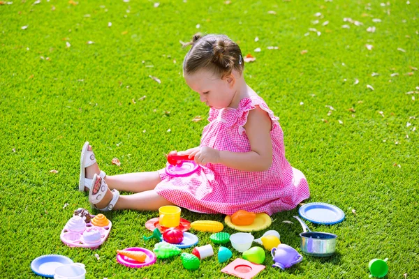 Menina criança brincando com brinquedos de comida sentados no relvado — Fotografia de Stock