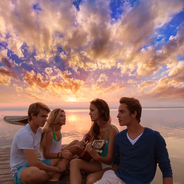 Groep vrienden op zonsondergang strand plezier met gitaar — Stockfoto