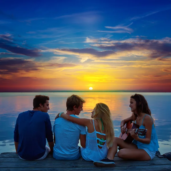 Groep vrienden gitaarspelen in zonsondergang pier in de schemering — Stockfoto
