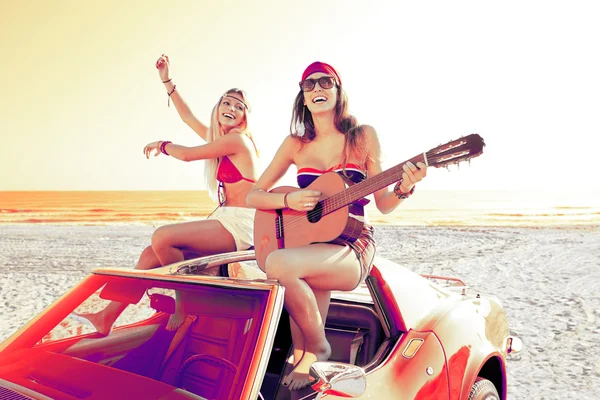 Girls having fun playing guitar on th beach in a car — Stock Photo, Image