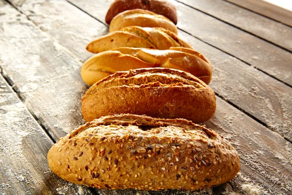 Breads varied in a row on rustic wood and flour — Stock Photo, Image