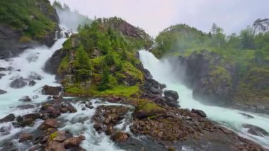 Güçlü Latefossen şelalesi Parlak bir yaz gününde Norveç 'teki taş köprü arkasında.