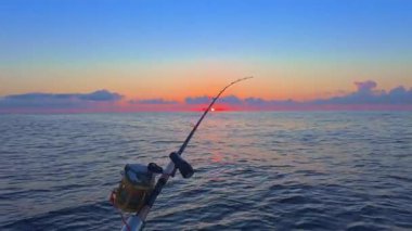 Gün batımında açık denizde balık avlamak, altın ufuk ve sakin okyanusla botta olta ve makaralar..
