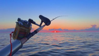 Gün batımında açık denizde balık avlamak, altın ufuk ve sakin okyanusla botta olta ve makaralar..