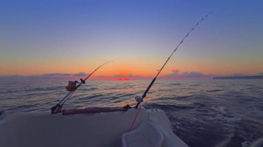 Gün batımında açık denizde balık avlamak, altın ufuk ve sakin okyanusla botta olta ve makaralar..