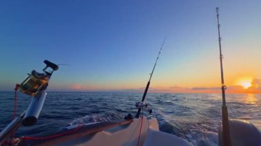 Gün batımında açık denizde balık avlamak, altın ufuk ve sakin okyanusla botta olta ve makaralar..