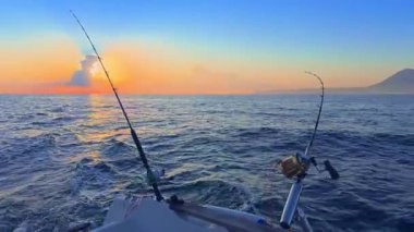 Gün batımında açık denizde balık avlamak, altın ufuk ve sakin okyanusla botta olta ve makaralar..