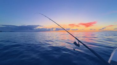 Gün batımında açık denizde balık tutmak, sakin denizde olta atmak, mürekkep balığı ve kaya türleri için altın ufuk.
