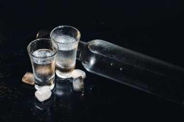 Siyah şişenin ve votka bardaklarının yakından görüntüsü.