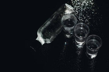Siyah arka planda shot bardaklarında votka, sisli bardakta buzlu sert içki.
