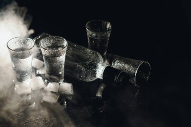 Siyah şişenin ve votka bardaklarının yakından görüntüsü.
