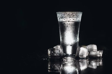 Siyah arka planda shot bardaklarında votka, sisli bardakta buzlu sert içki.
