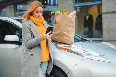 Elektrikli benzin istasyonunda elektrikli araba şarj ediliyor. Arabanın yanında duran kadın..