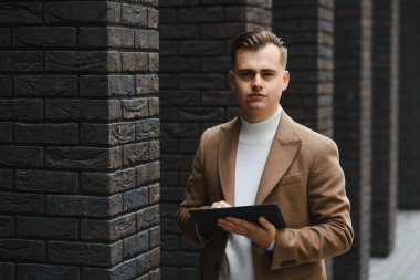 Şehir caddesinde tablet bilgisayar kullanan yakışıklı bir iş adamı. Siyah takım elbiseli, güneş gözlüklü şık bir erkek model.