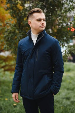 Genç, yakışıklı bir adamın portresi, moda modeli, şehir arka planında modern saç stili, gündelik kıyafetler giyiyor..