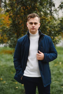 Genç, yakışıklı bir adamın portresi, moda modeli, şehir arka planında modern saç stili, gündelik kıyafetler giyiyor..