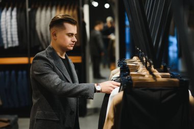 Bir kostüm dükkanındaki genç ve yakışıklı işadamı askıdaki ceketin kolundaki kumaşı inceliyor..