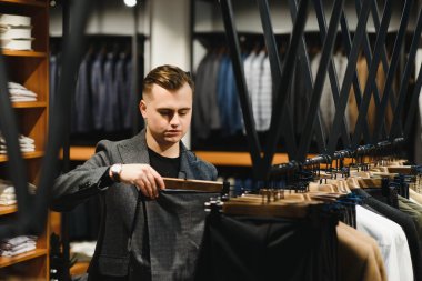 Bir kostüm dükkanındaki genç ve yakışıklı işadamı askıdaki ceketin kolundaki kumaşı inceliyor..