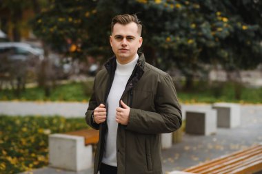 Genç, yakışıklı bir adamın portresi, moda modeli, şehir arka planında modern saç stili, gündelik kıyafetler giyiyor..