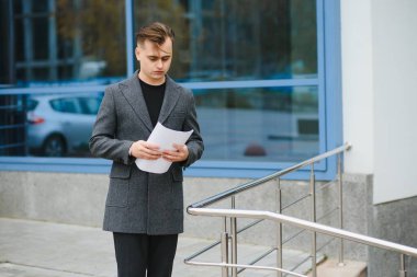 Sokakta evrak okuyan ciddi bir iş adamı. Evrakları dışarıda inceleyen kendine güvenen bir iş adamı. Şehir caddesinde belgelerle dolaşan düşünceli bir adam..