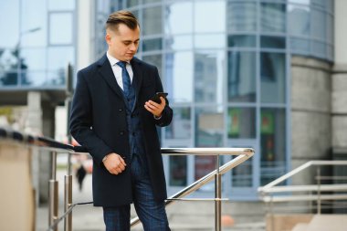 Ofis binasının yanında duran yakışıklı iş adamı cep telefonuyla iş görüşmesi yapıyor.