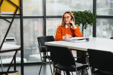 İşte gülümseyen iş kadını telefonda konuşuyor, iş yerinde oturuyor, fotokopi çekiyor.
