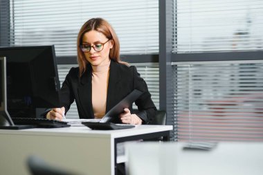 Genç iş kadını işyerinde oturuyor ve ofiste gazete okuyor.