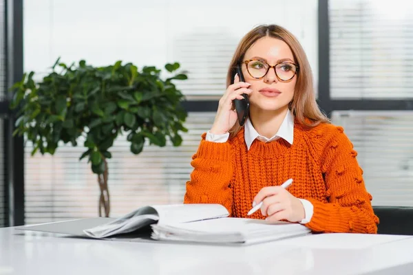 Happy smiling business woman at work talking on phone, sitting at her working place in office, copy space