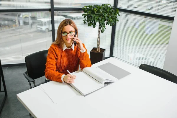 Happy smiling business woman at work talking on phone, sitting at her working place in office, copy space