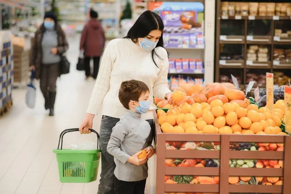 Mom and son wearing protective masks choose fruits to buy in the store