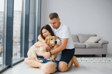 Mutlu Aile Kavramı. Modern apartmanda yerde oturan köpekli güzel bir çiftin portresi.