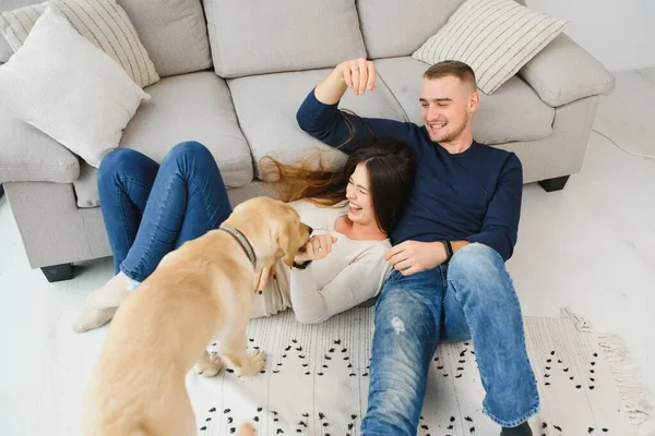 Young couple with a dog at home. Young man and a woman playing at home with dog.