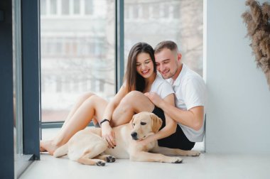 Mutlu Aile Kavramı. Modern apartmanda yerde oturan köpekli güzel bir çiftin portresi.