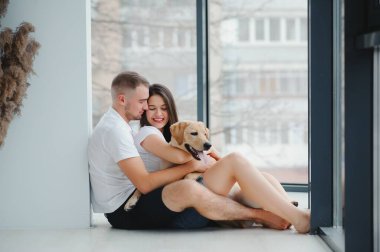 Genç mutlu çift yeni bir eve taşınıyor. Yeni evlerine kutular dolusu eşya getirdikten sonra yerde köpek yavrusuyla oturuyorlar..